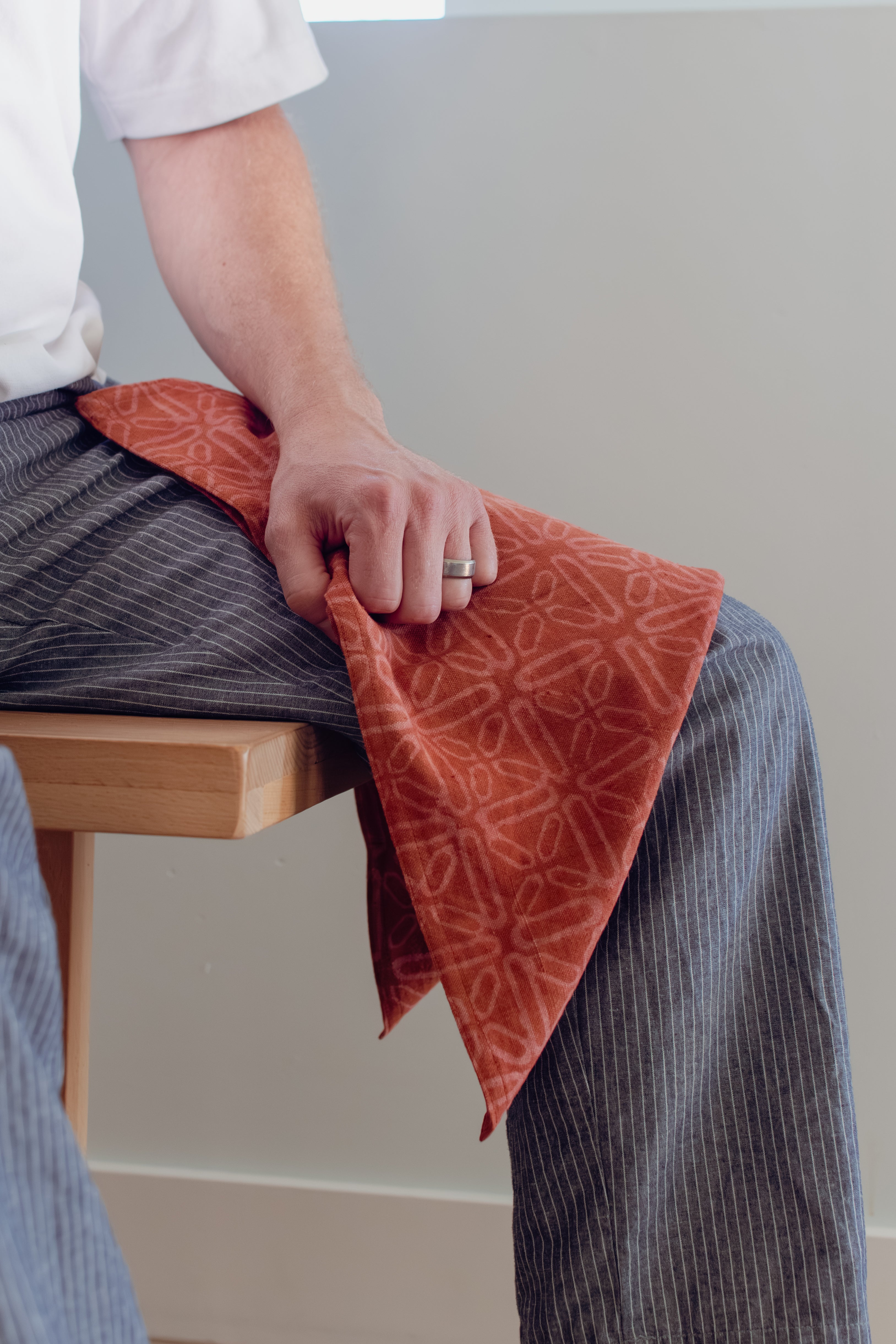 Person sitting on a wooden bench with a red patterned cloth draped over their lap against a plain background