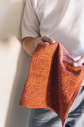 Person holding a folded red-orange napkin with geometric patterns against a neutral background
