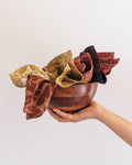 Hand holding a wooden bowl with a set of patterned cotton cloths against a light background