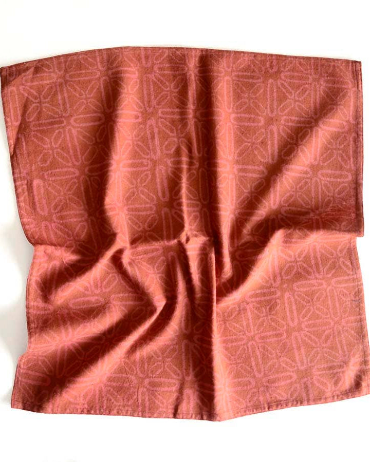 Slightly crumpled geometric red-orange cotton napkin on a white background